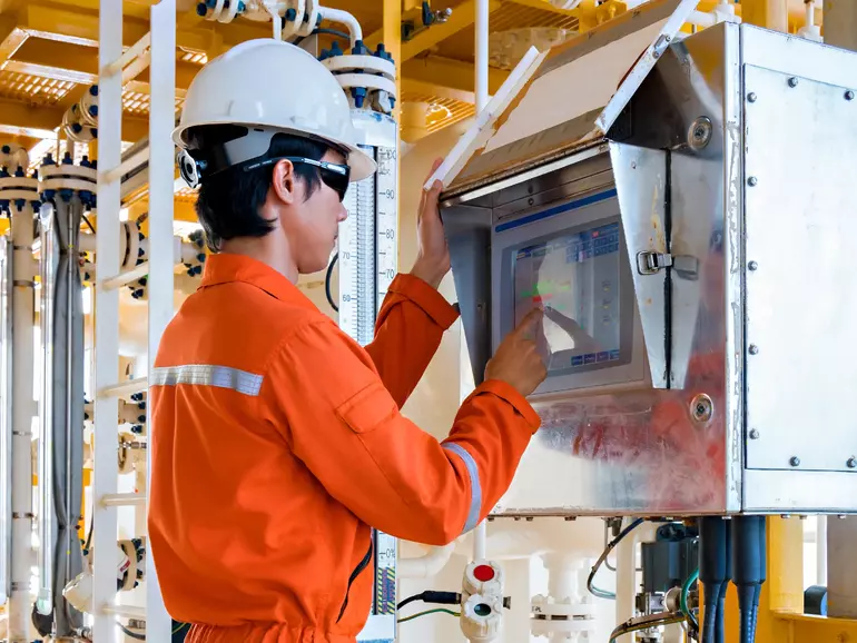 Ein Arbeiter auf einer Bohrinsel bedient ein Ventil über ein Touchscreen-Panel, um das Öffnen und Schließen des Ventils auf einer entfernten Öl- und Gasplattform zu steuern.