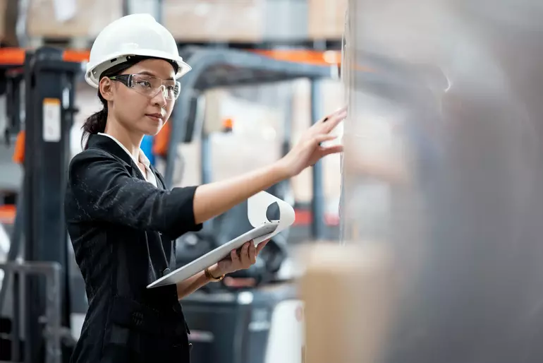Eine junge Frau in einer Polohemd-Uniform, die die Produkte in einem Regal überprüft, asiatisches Personal, das in einem Vertriebslager und einer Supply-Chain-Management-Lösung Inventur macht